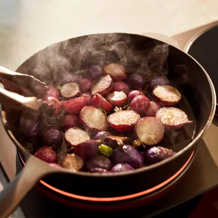Radishes sizzling in a pan on a lit burner